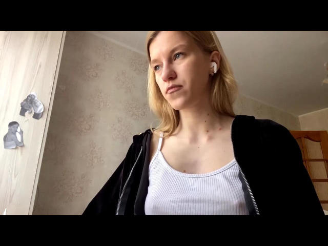 DeedraGalarneau has blonde hair, white earbuds, a black zip-up jacket, and a white ribbed tank top. Her tits are small and visible through the top.