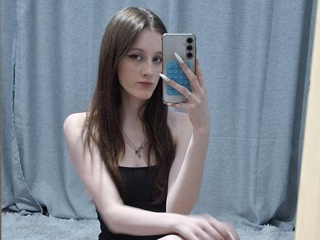 LeticiaEttl with long brown hair, wearing a black strapless top, holding a blue phone case, taking a mirror selfie, showing her pale skin and small tits.