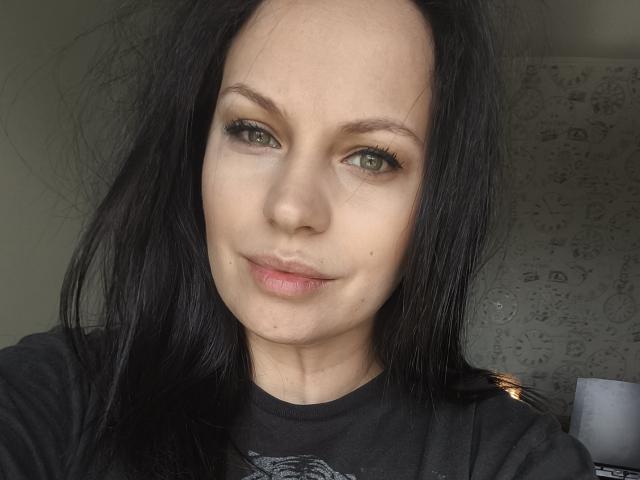MadisonTayler69 hat helle Haut, grüne Augen, schwarzes, glattes Haar und trägt ein schwarzes T-Shirt. Sie hat ein leichtes Lächeln und leicht geschwollene, rosafarbene Lippen..
