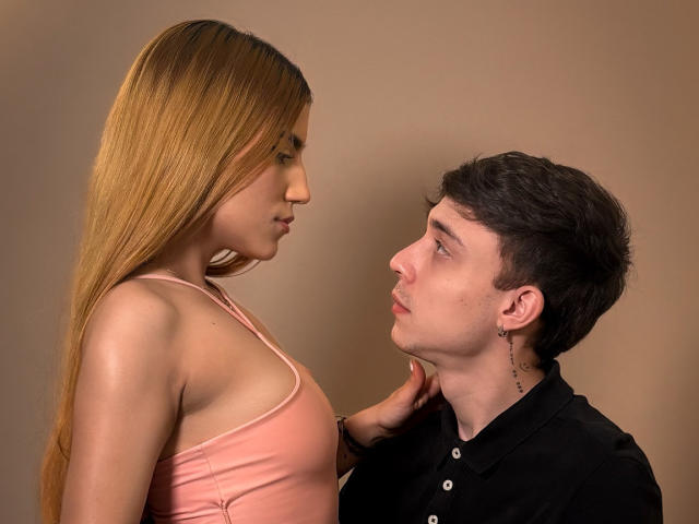 SecretLoversVIP con lunghi capelli biondi, vestita con una maglietta rosa, in piedi, che guarda verso il basso SecretLoversVIP con capelli castani corti, una maglietta nera, orecchini, che guarda verso l'alto, con una mano al collo..