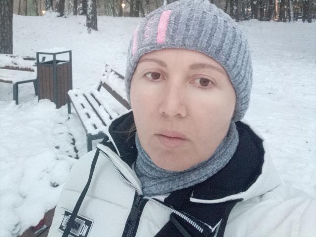 ZoyaPask, con un gorro de punto gris con una franja rosa y una bufanda gris, lleva una chaqueta blanca, tiene una expresión neutra, y en el fondo se ve un parque cubierto de nieve..