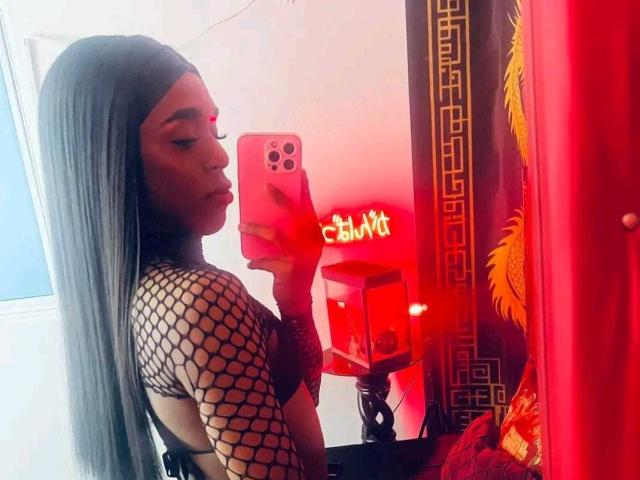 NashlaLonga with long black hair, fishnet top, red lipstick, holding pink phone, side profile, red neon "Chill" in background, red curtains with gold patterns.