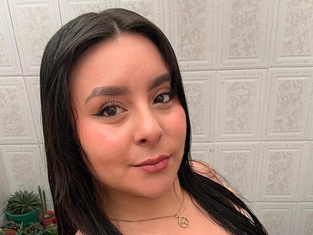 EmaJames has dark straight hair, brown eyes, and a cute face with light makeup and a subtle smile. She's wearing a necklace with a small circular pendant.