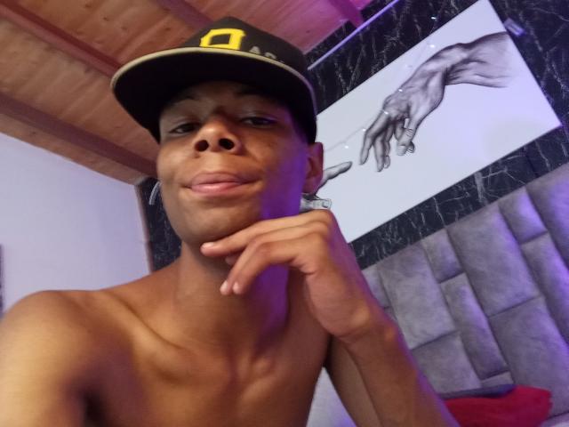 MasterXx, shirtless with a dark baseball cap, brown skin, and a cute smile, rests his chin on his hand, showing his nose and lips. Black and white hand art.