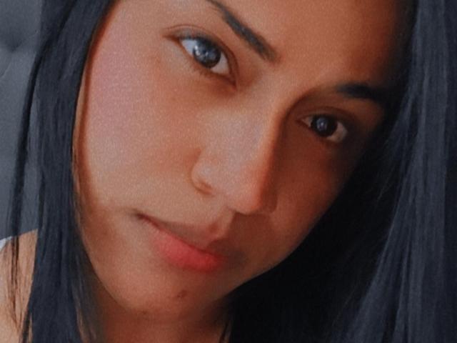 IvannaDuran's face with a slight smirk, dark straight hair, blue eyes, and a light brown skin tone, showing a subtle nose and full lips. Her ass is not visible.