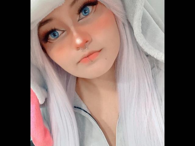 LuckyLeahh mit blauen Augen, weißem Haar und einem Nasenring, trägt einen flauschigen weißen Hut und sieht süß und leicht errötend aus. Ihre Lippen sind leicht geöffnet..