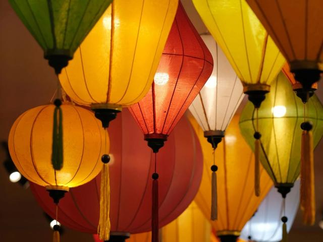 Un gruppo di lanterne colorate appese, con paralumi gialli, rossi, verdi e bianchi, illuminate dall'interno, che creano un'atmosfera calda, festosa e leggermente sensuale..