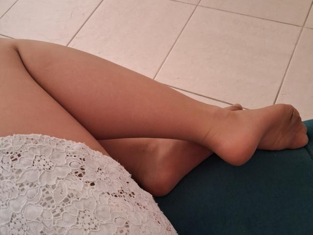 Marriam's bare legs crossed, showing smooth, tan skin with a lace white skirt bottom, resting on a blue cushion, white tiled floor in the background.