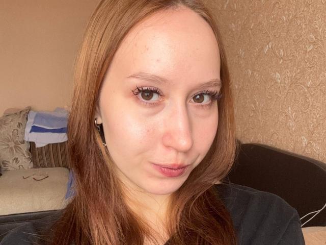 Linn Schwartzberg mit hellbraunen Haaren, heller Haut, einer kleinen Nase und braunen Augen, trägt ein schwarzes Hemd, hat einen leichten Schmollmund, kleine schwarze Ohrringe und dezentes Make-up, und befindet sich in einem gut beleuchteten Raum..