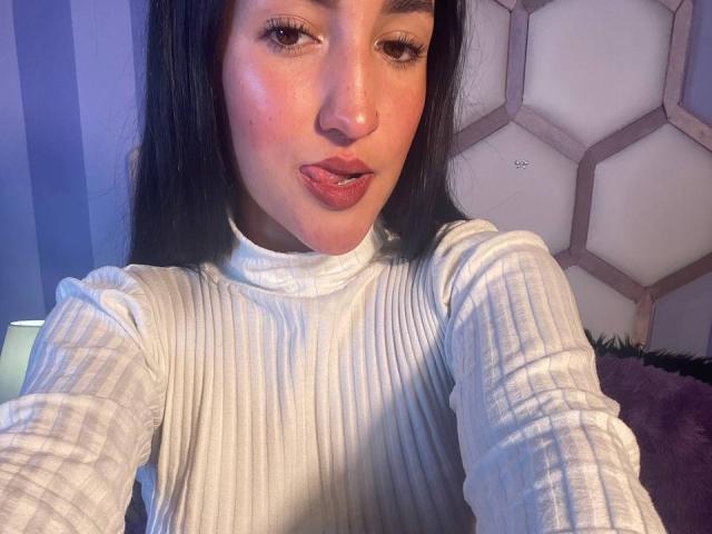 YviTaylor with long black hair, pouty pink lips, and white ribbed turtleneck, looking at camera with slightly parted lips. Her ass is not visible.