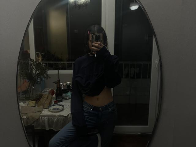 Sashenka69, vestindo um suéter azul marinho escuro, levantando-o para mostrar sua barriga nua, usando jeans azuis, tirando uma selfie no espelho com o celular, cobrindo o rosto..
