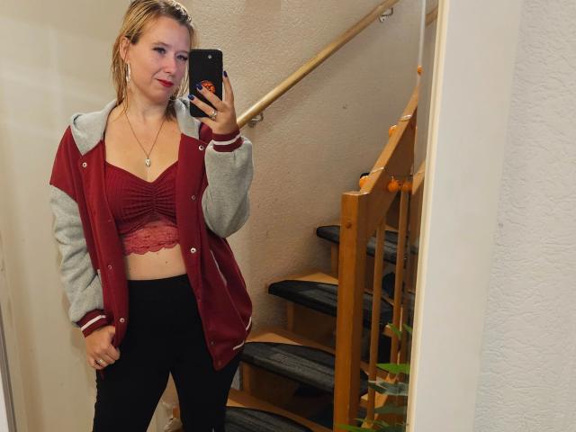 Lea-sommer-hot with wet blonde hair, red lace top, black pants, and red-gray jacket, taking a mirror selfie, showing her tits and ass, in a stairway.