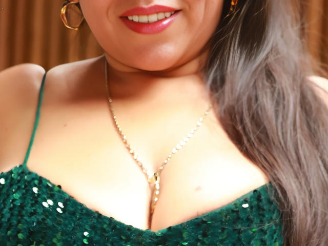 VeraCruz, met een groene jurk met pailletten, een gouden ketting en rode lippenstift, glimlacht ze licht. Haar bruine haar bevindt zich aan de rechterkant..