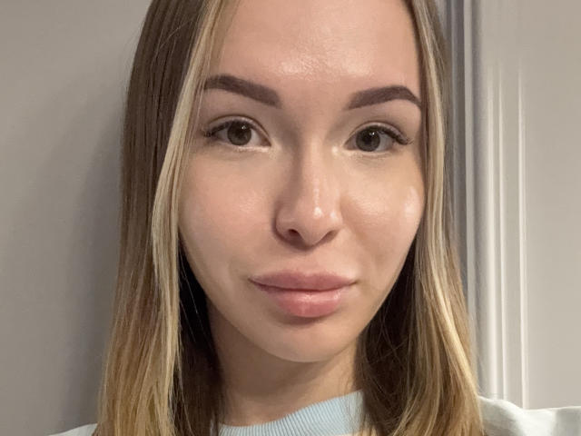Donya Gyllensten hat ein glattes, glänzendes Gesicht mit hellbraunen, glatten Haaren, brauen Augenbrauen und rosafarbenen Lippen. Sie trägt ein hellblaues Oberteil und blickt direkt in die Kamera..