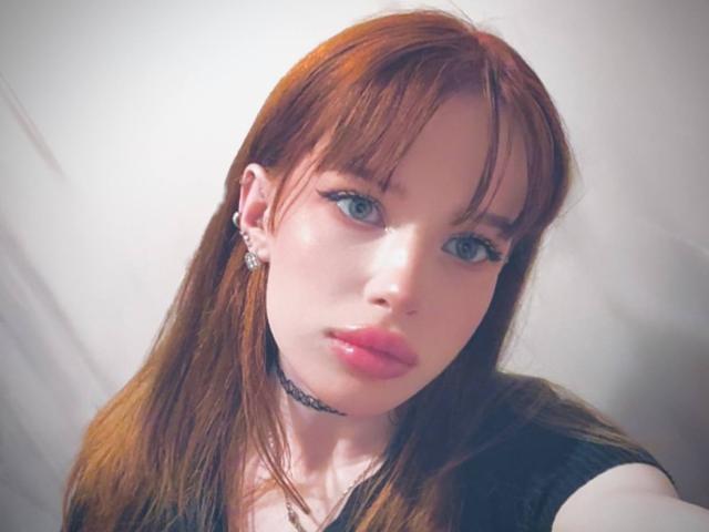Margo Tamminen hat rotes Haar, blaue Augen und rosafarbene Lippen. Sie trägt ein schwarzes Oberteil mit einem Choker, Ohrringen und einer Halskette und blickt mit ernstem Gesichtsausdruck direkt in die Kamera..