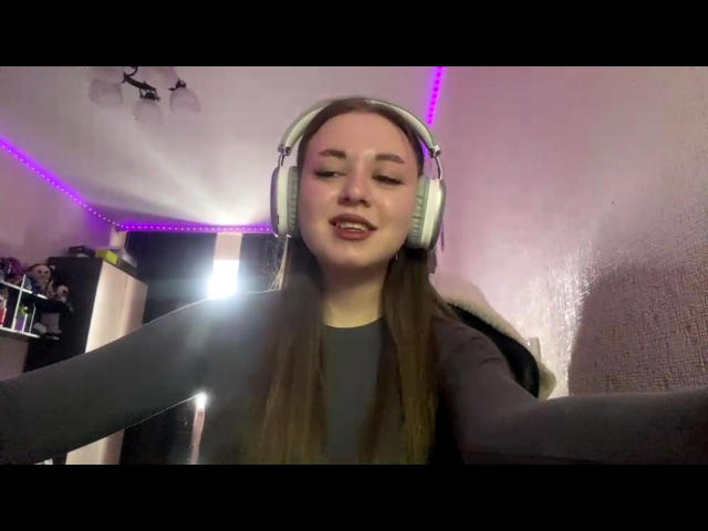MartiSawdo with long brown hair, wearing gray shirt and large white headphones, smiling slightly, with purple LED lights in background. MartiSawdo's face is centered, arms out.