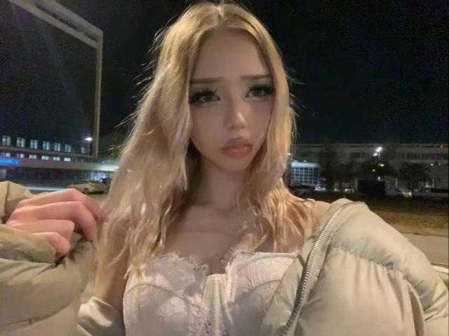 JoelHoefer with blonde hair, wearing a white lace bra, green puffy jacket, and serious expression, night setting, hand in jacket, visible tits, soft lighting, slightly wavy hair.