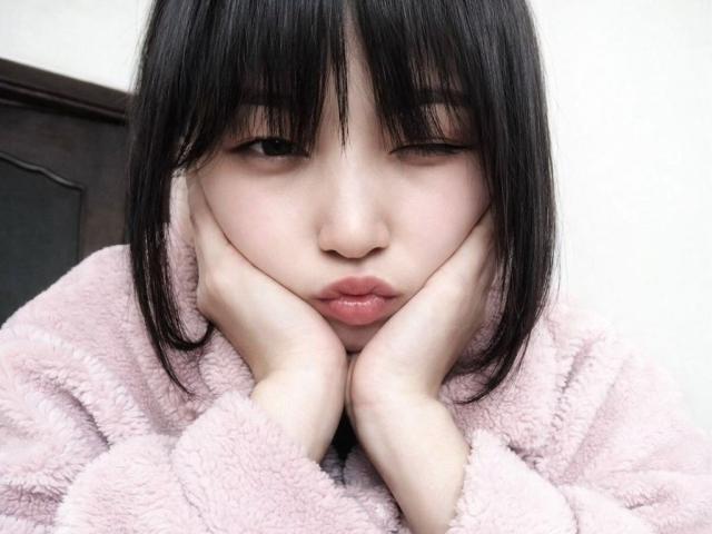 GeorgiaVondoloski with black hair, pouty pink lips, hands under chin, wearing a pink fuzzy sweater, looking tired and cute.