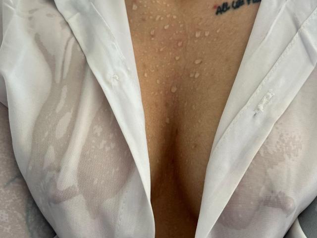 GiaMoretii's wet white shirt clinging to her tits, water droplets on her chest, visible nipples, and a tattoo above her right breast. Her shirt is open, showing cleavage.