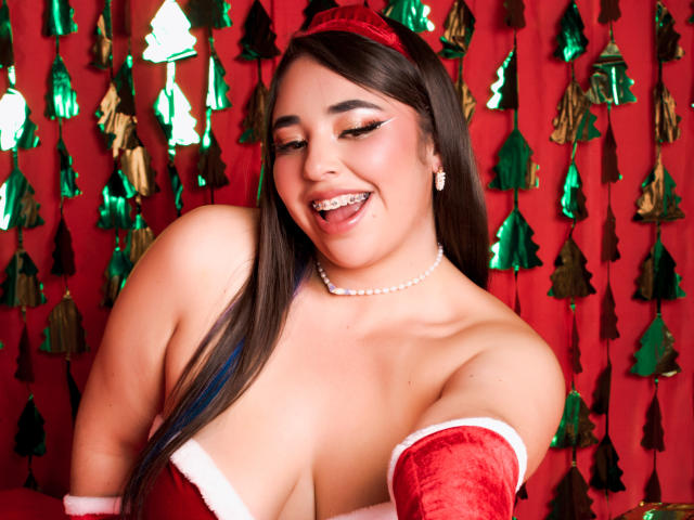 BaGiolett with dark hair, red headband, and red gloves, showing off her big tits, smiling with tongue out, wearing a pearl necklace, and Christmas-themed.
