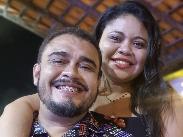 BigCoupleBr, um sujeito corpulento com barba e cabelo curto e cacheado, e a namorada atraente de BigCoupleBr, com pele brilhante e cabelo castanho longo, sorrindo juntos..