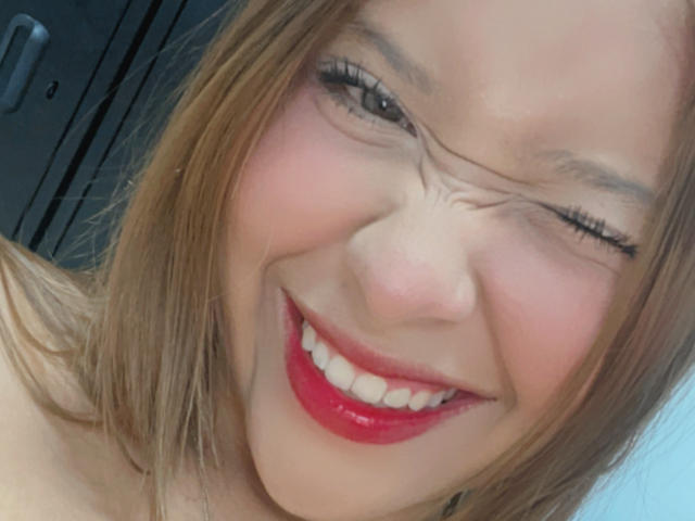 HeraJuno's face is in the shot, winking with a goofy expression, red lips, and a slight smile, showing off her teeth and a hint of her ass.