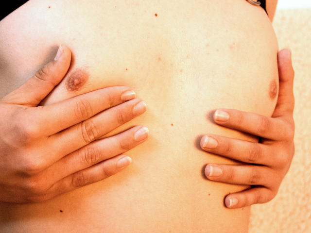 AxelLaciel's bare tits, hands covering them, light skin, small brown nipples, and neatly trimmed fingernails, in a warm-colored, textured background.