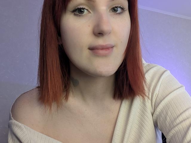 DiamondLeanos heeft bleke huid, rood haar dat tot op haar schouders reikt, en draagt een crèmekleurig topje met een open schouder. Ze kijkt naar de camera met een lichte glimlach en laat een kleine, donkere tatoeage zien..
