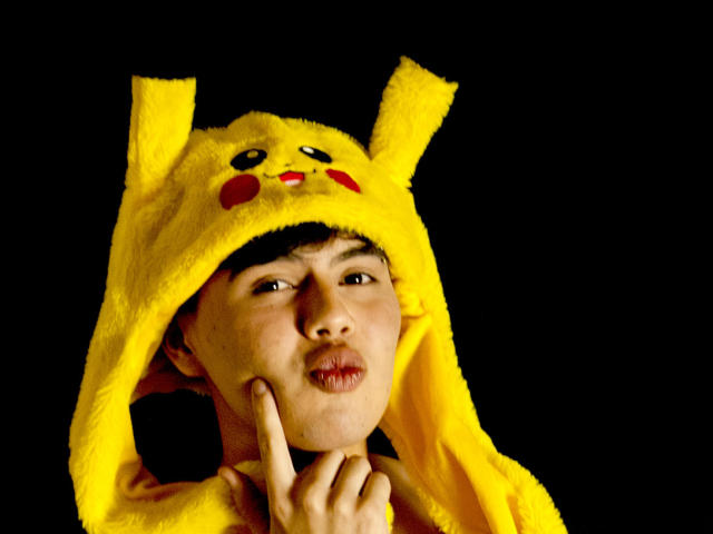  FelipeKold wearing a Pikachu yellow hat with ears, puffy cheeks, and red nose, making a pouty face with finger on chin, against a black background.