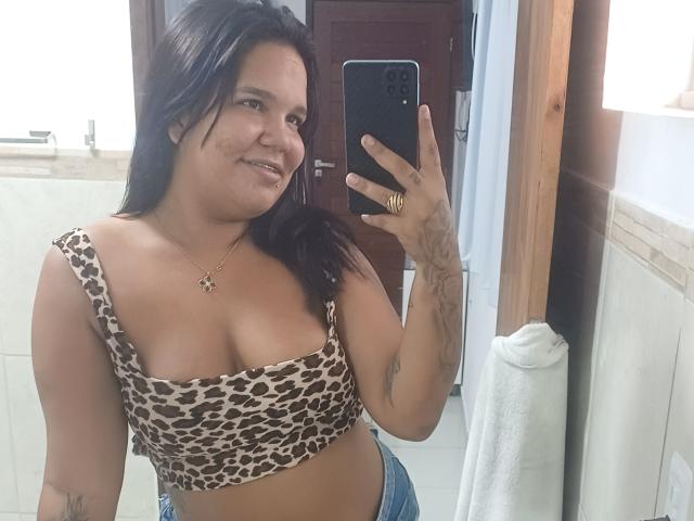 TaniyaS with medium tits in a leopard print crop top, smiling, holding a phone in a bathroom mirror selfie, has tattoos, and wears blue jeans.