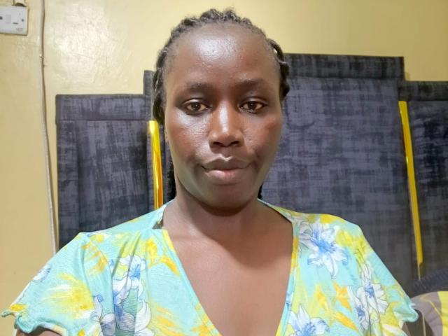 NanaMarlene with dark brown skin, small nose, and short braided hair, wearing a green floral dress, has a subtle smile and visible pores on her face.