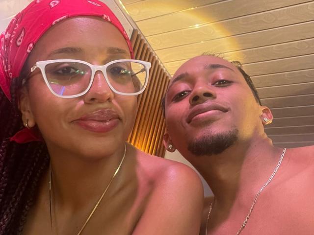 LilithAndAsmodeo with glasses, red bandana, and pouty lips, next to LilithAndAsmodeo with short hair and goatee, both wearing earrings and necklaces, smiling at the camera.