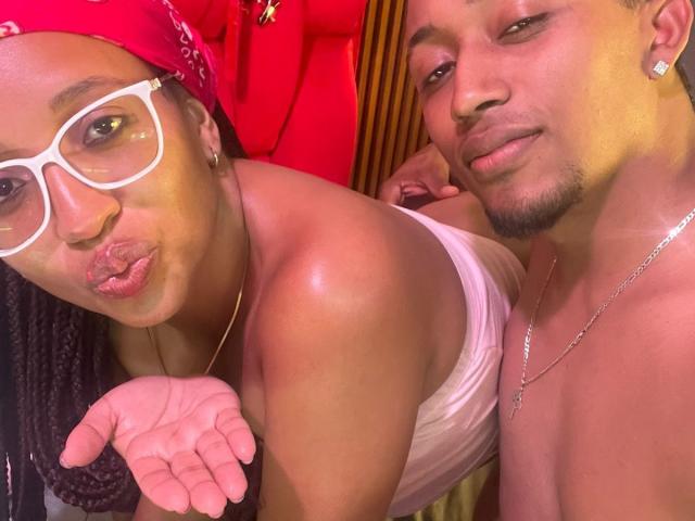 LilithAndAsmodeo with braids, white glasses, red bandana, pouty lips, and raised hand, next to shirtless LilithAndAsmodeo with earring, necklace, and slight smile.