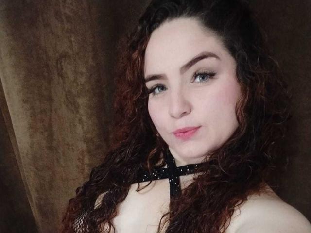 AmandaWt ha i capelli castano ricci, la pelle chiara e indossa una maglia nera in rete con spalline incrociate. Ha gli occhi azzurri, le labbra rosa e un leggero sorriso..