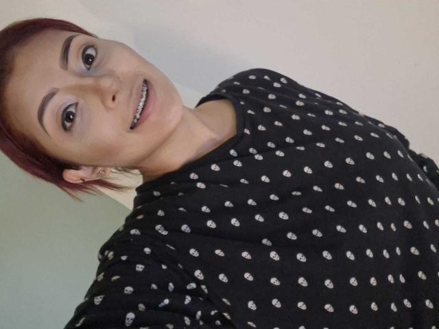LizBonnet has short red hair, dark eyebrows, and a cute smile showing small teeth. She's wearing a black polka dot shirt, looking up at the camera.