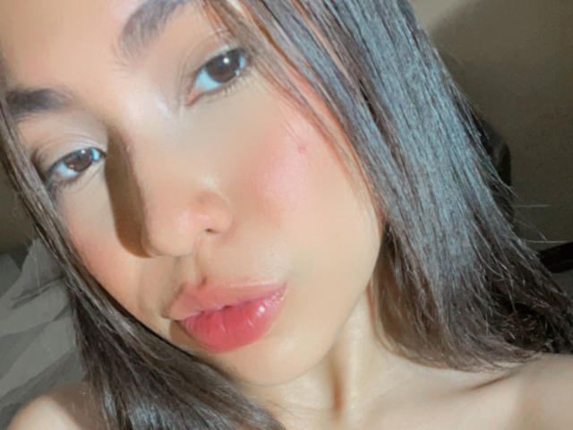 Angels69v's face with shiny brown hair, pouty pink lips, and a slight blush on her cheeks. She's looking up with dark, shiny eyes. Her skin is smooth and tan.