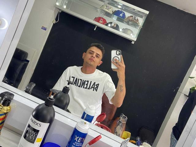 JenniDamian tirando uma selfie em um espelho, vestindo uma camiseta branca com a inscrição "PANAMENIO", com uma garrafa preta, uma lata azul e uma escova de dentes vermelha sobre a superfície branca do espelho..