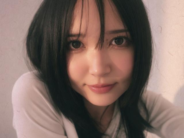EmaVanhowe has straight black hair, large brown eyes, and a gentle smile with pink lips. She's wearing a white shirt, looking directly at the camera with a cute expression.