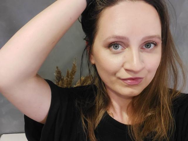 KristalSoetux heeft een lichte huid, blauwe ogen en bruin haar, draagt een zwarte blouse, met één arm omhoog, en heeft een lichte glimlach, met een roze lippenstift..