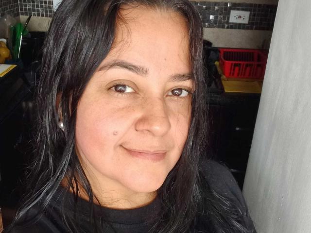 VonneLucia has dark brown eyes, straight black hair, light brown skin, small mole on the right side of her nose, and a slight smile. She's wearing a black shirt.