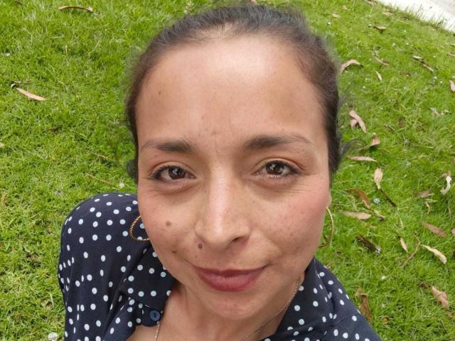 StangelarRivera tiene una cara linda con ojos marrones, una nariz pequeña y una sonrisa sutil. Lleva una camisa de lunares y su cabello oscuro está recogido. No se ven los senos..