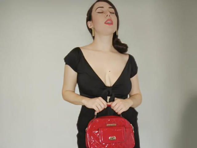 MabyLegrand with closed eyes, red lipstick, black dress, deep cleavage, holding red glossy backpack, brown hair in ponytail, white background.