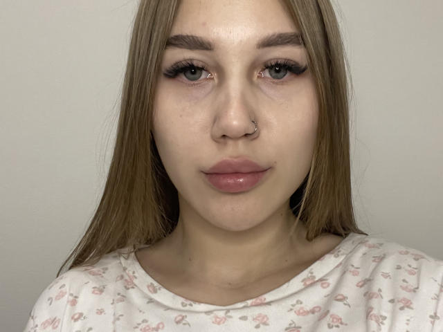 A SleepyNudy tem cabelo castanho liso, usa um piercing no nariz e veste uma camisa branca com estampas florais. Ela tem lábios rosados, olhos verdes e delineador preto grosso. Suas nádegas não estão visíveis..
