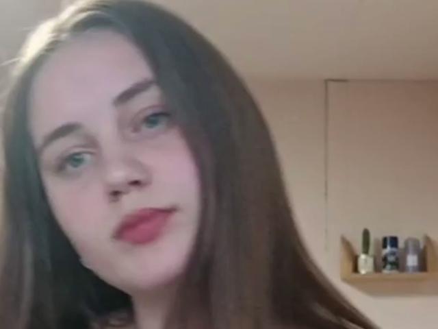 AlysiaFinkelstein heeft bleke huid, lang bruin haar en rode lippenstift, en kijkt iets opzij met een neutrale uitdrukking op een onscherpe selfie. Haar borsten zijn niet zichtbaar..