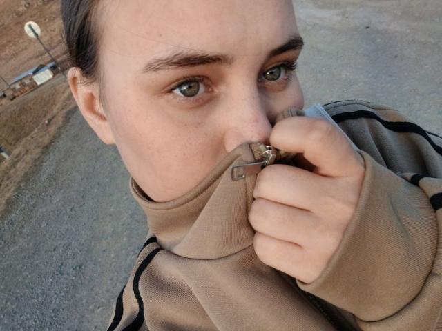 Alysia Finkelstein, con gli occhi verdi, indossa una felpa beige con zip e si copre la bocca con una mano. Ha la pelle chiara, i capelli castani e un viso leggermente lentigginoso..