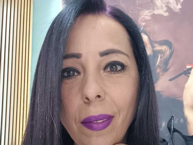 LauraSin has dark, straight hair, purple lipstick, and black eyeliner with long lashes. Her eyes are gray, and she's smiling softly. Her ass is not visible.