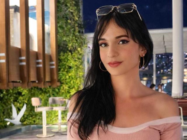 PamelaKander with black hair, wearing a pink off-shoulder top, gold hoop earrings, and sunglasses on her head, has a cute face and small tits.