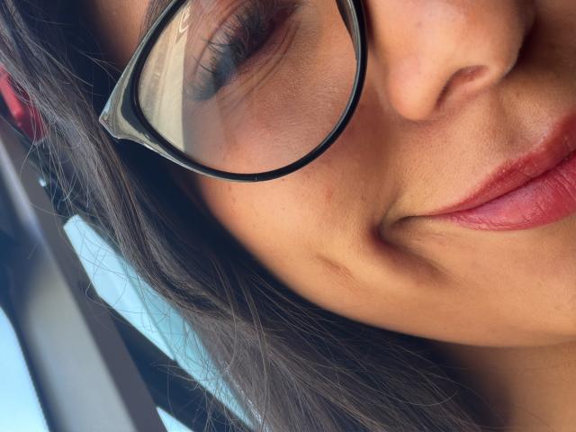 SarahPrincess's face with brown skin, dark brown hair, and red lipstick, wearing black glasses, smiling slightly, eyes closed, and nose visible. Her tits are not shown.