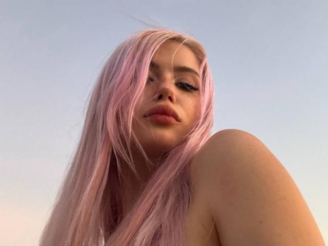 Anabel Tanberg ha i capelli rosa, labbra piene e un naso leggermente all'insù. Si vede una spalla e sta guardando in basso con un'espressione sottile e sicura..