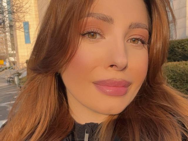 MiraVolt has brown eyes, full pink lips, and light brown wavy hair. She's wearing black, with a slight smile and no makeup. Her tits are small, her ass is unseen.